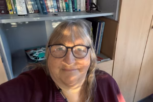 Andrea Sam vor einem Bücherregal, nachdenklich und klar, mit Lichtreflexion in der Brille – passend zum Artikel über Kommunikationstrends 2026.