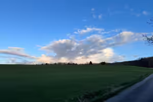 Klarer blauer Himmel mit weißen Wolken über einer weiten grünen Landschaft
