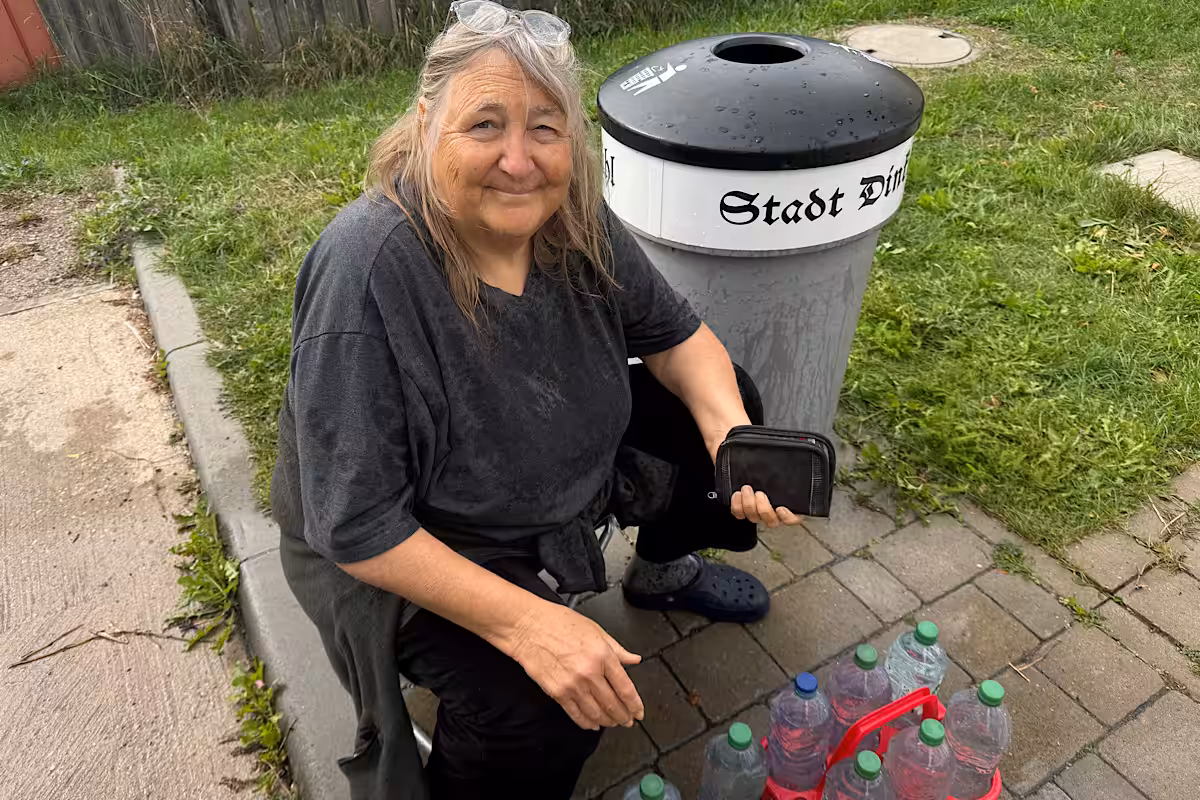 Frau kniet neben einem Mülleimer mit einer Kiste Wasserflaschen