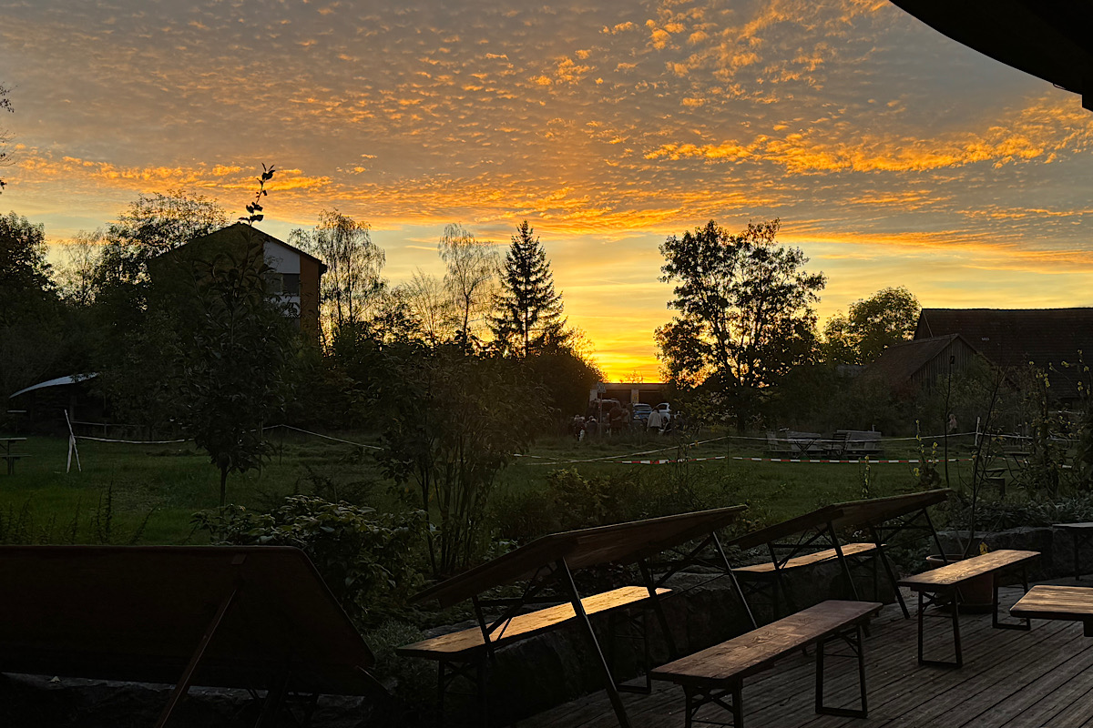 Terrasse mit Bierbänken, auf der die Gemeinschaft am Tempelhof sitzt und isst, im Abendlicht